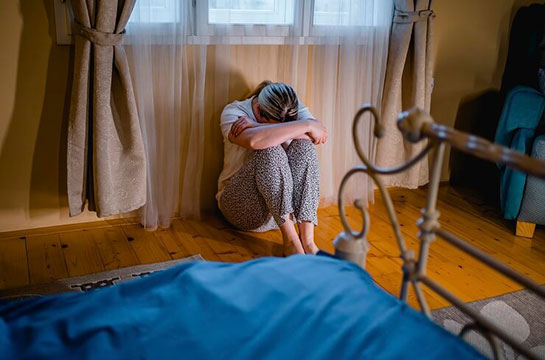 Woman sitting alone on bedroom floor